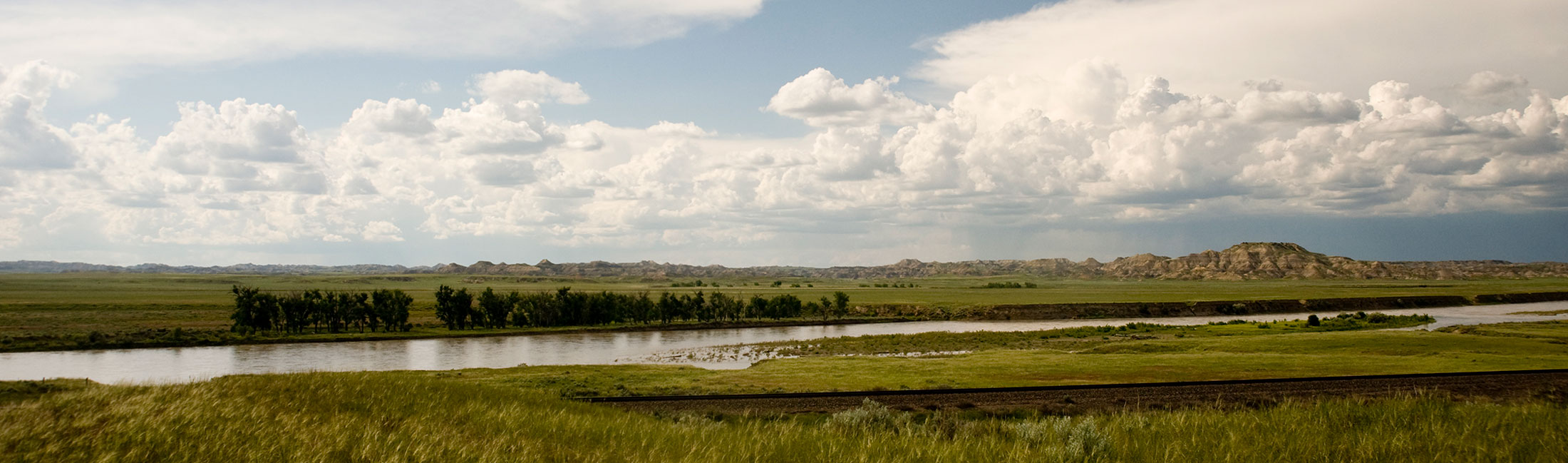 yellowstone river with green grass, trees, foothills and clouds