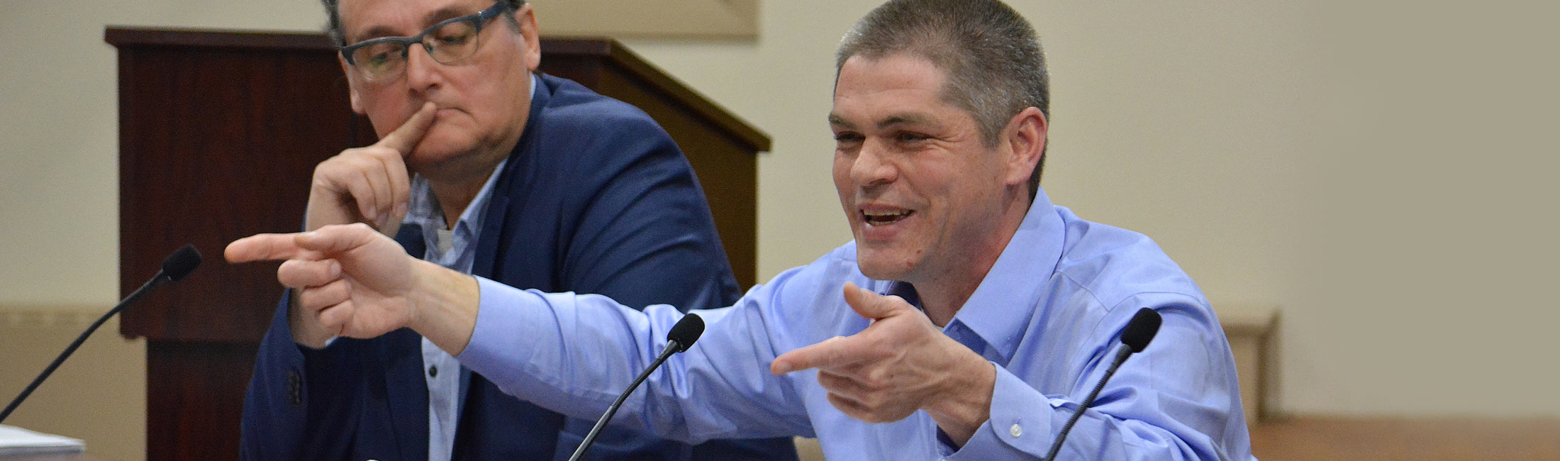 man seated speaking into microphone at meeting