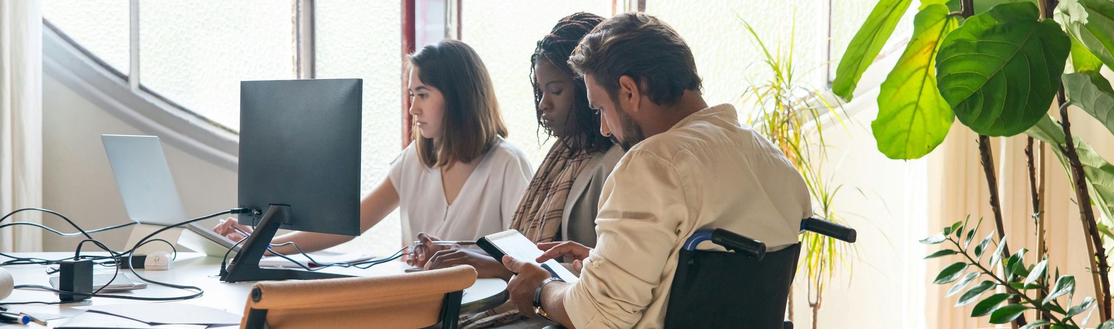 man in wheelchair sitting in a meeting with two women at desk