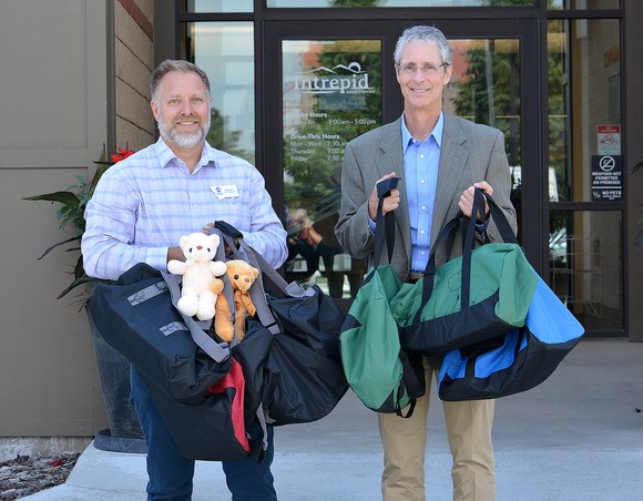 Rob Lawler, of the DPHHS Office of Faith and Community Based Services, and Intrepid CEO Greg Strizich with some of the donated duffel bags. 