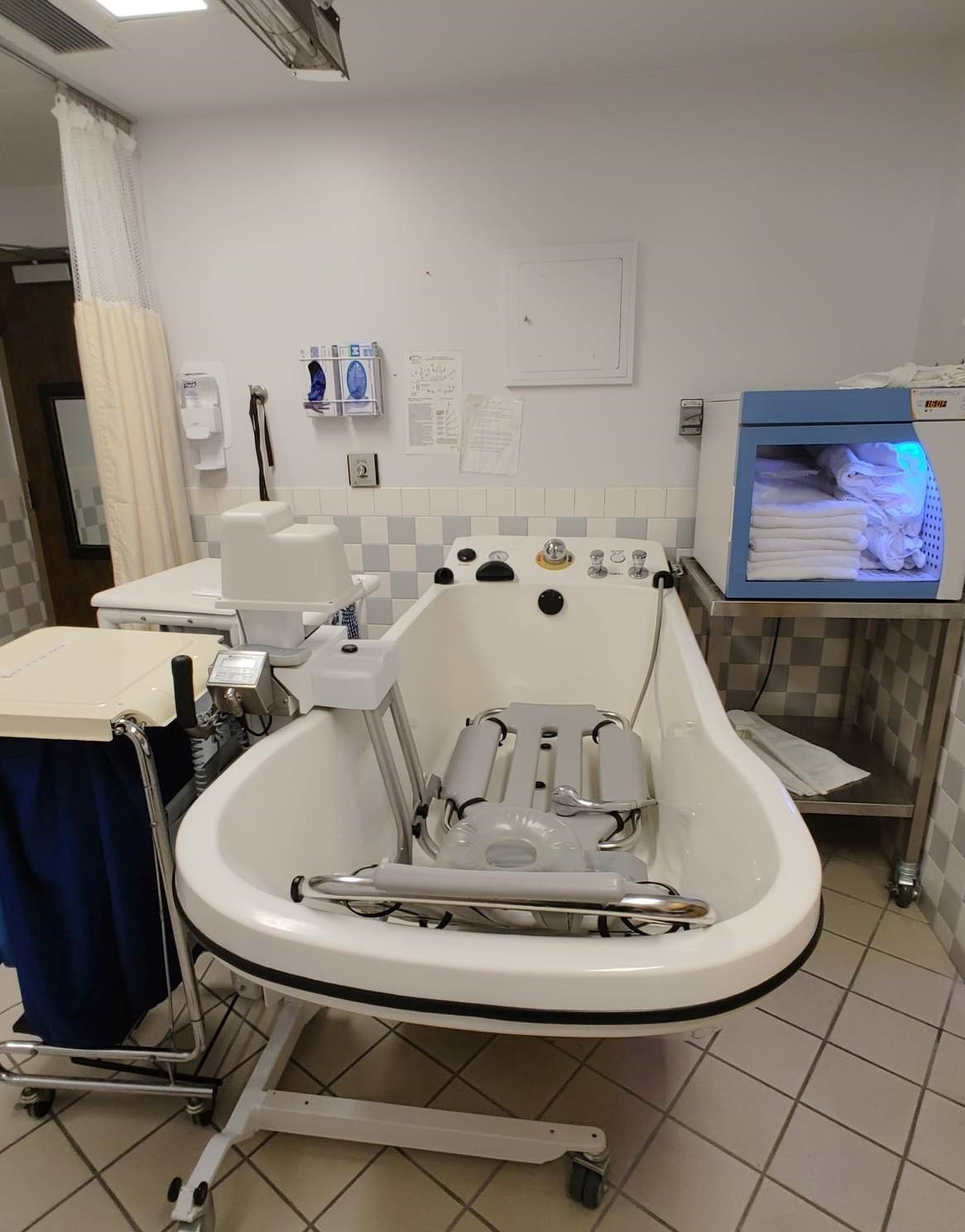 A picture of the shower room. There is a large tub with accessibility attachments.