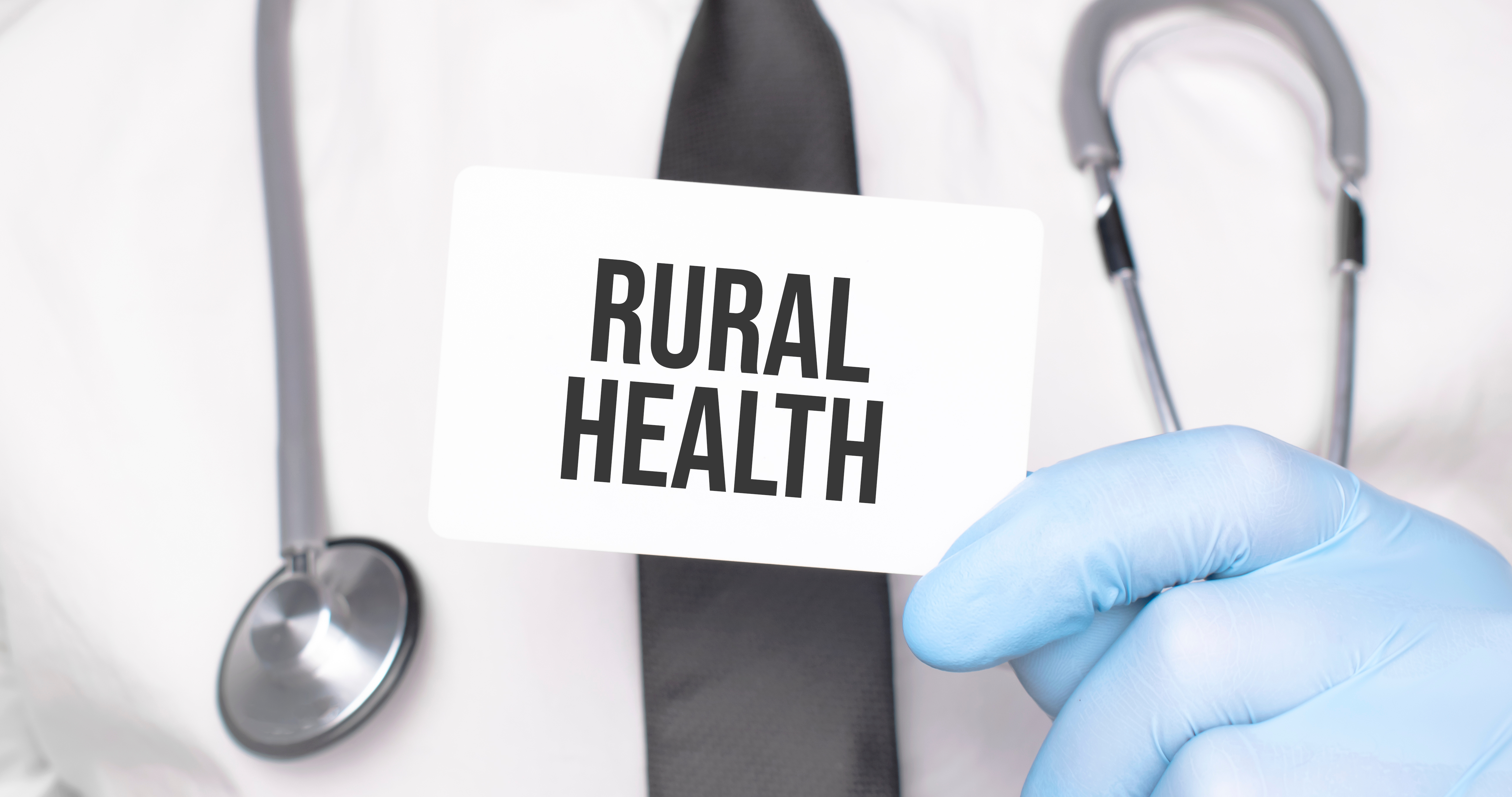 Photo of a doctor's torso with a stethoscope around their neck and holding a sign that reads, "RURAL HEALTH"